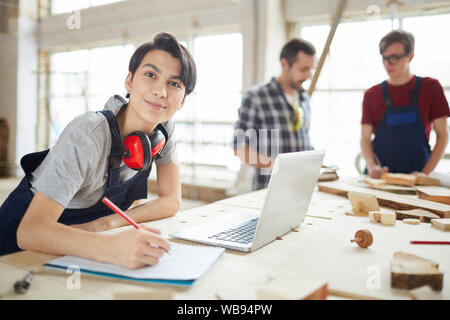 Portrait of modern carpenters working at woodworking factory, focus on young woman smiling at camera in foreground, copy space Stock Photo