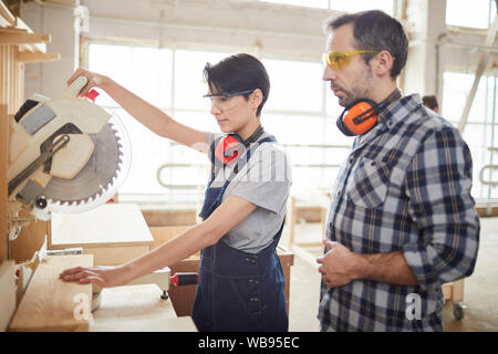 Side view portrait of mature carpenter helping young worker sawing wood in joinery, copy space Stock Photo