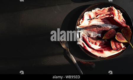 Tasty appetizing classic Italian ham with figs on plate on black wood background. View form above. Top view. Horizontal. With copy space for text Stock Photo