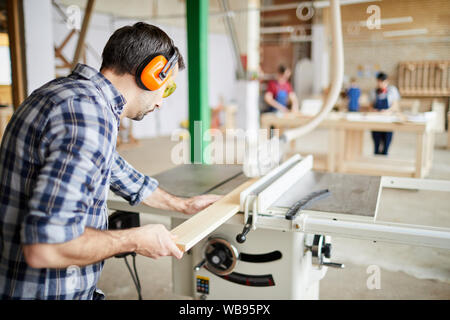 Back view portrait of mature carpenter cutting wood in joinery workshop, copy space Stock Photo