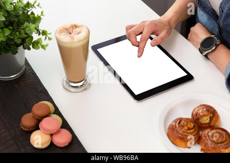 Woman with smartwatch using tablet in coffee shop. Coffee and pastry, macaroons on white table. Freelance working Stock Photo