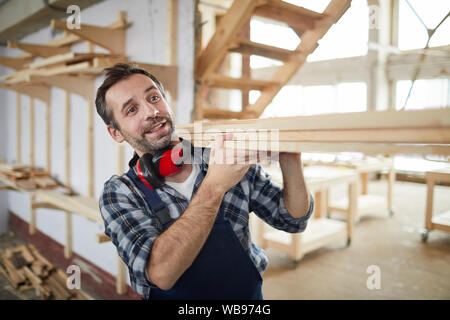 Waist up portrait of mature carpenter carrying wooden boards in industrial workshop, copy space Stock Photo