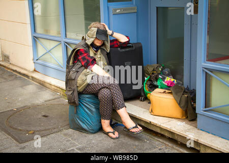 Paris, France - July 7, 2018: Homeless woman with bags and a suitcase on a street sidewalk in Paris Stock Photo