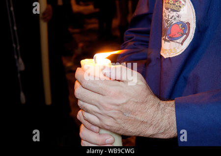 Closeup of the hands of a penitent nazarene holding his candle during a procession. Holy Week, Seville, Andalusia, Spain. Nocturnal procession of the Stock Photo