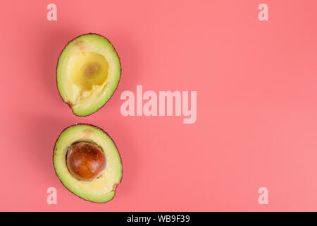 Two halves of avocado with stone on pink background.  Stock Photo