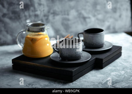 Transparent glass teapot with chitrus tea and cups, tea set on a wooden table. Close up, gray background, soft light Stock Photo