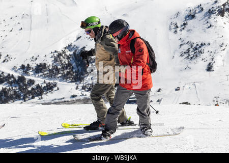 PYRENEES, ANDORRA - FEBRUARY 13, 2019: Two unknown skiers on the side of a mountain. Sunny winter day, ski slope in the background Stock Photo