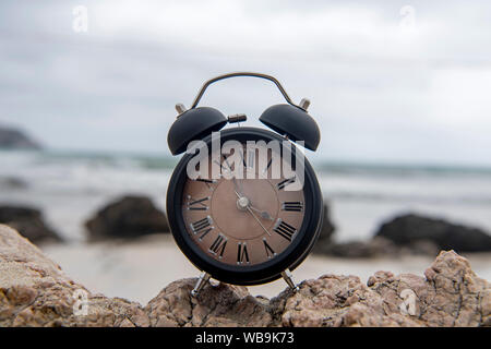 Alarm clock on a rock in the sunrise by the ocean Stock Photo
