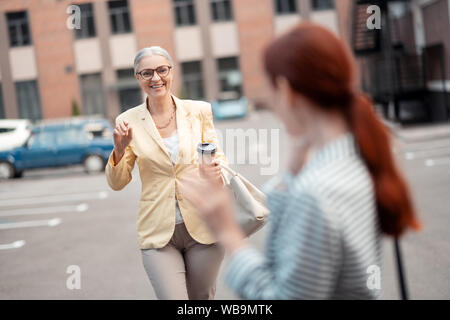 Pleased grey-haired business lady walking towards her friend Stock Photo