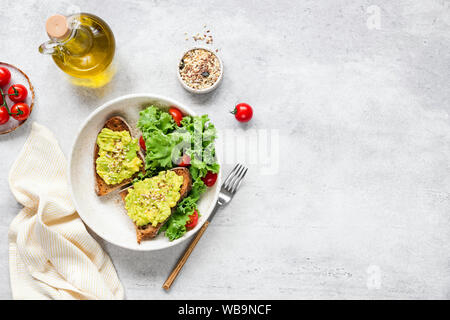 Avocado toast served with fresh green salad of kale, olive oil and tomatoes. Vegan, vegetarian food. Grey concrete background, table top view and copy Stock Photo