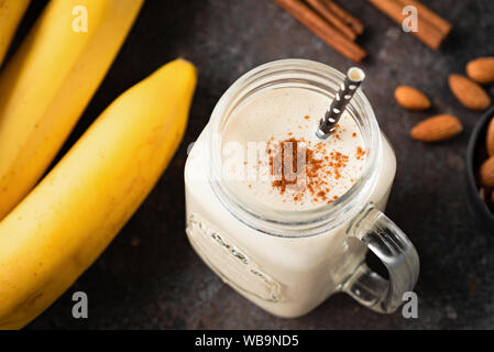 Healthy banana cinnamon smoothie or shake in glass cup on dark background. Top view, selective focus Stock Photo