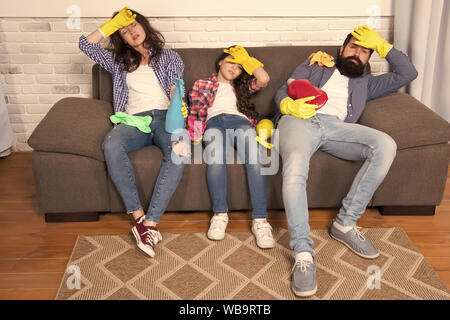 Cleaning all day exhausting occupation. Tired parents and kid. Exhausting cleaning day. Family mom dad and daughter with cleaning supplies sit on couch. Family care about cleanliness. Finish cleaning. Stock Photo