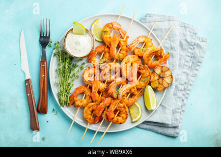 Grilled shrimp skewers or langoustines served with lime, garlic and sauce on a light blue concrete background. Seafood and beer. Top view. Flat lay Stock Photo