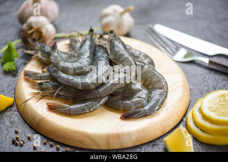 raw shrimps on wooden cutting board plate / fresh shrimp prawns for cooking with spices lemon and celery garlic on dark background in the seafood rest Stock Photo
