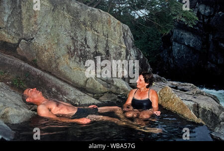 An adult couple relaxes in one of nine separate hot springs that are part of Baranof Warm Springs, an isolated tourist destination on Baranof Island in the Alexander Archipelago along the panhandle of southeast Alaska, USA. Located on same island as the Inside Passage community of Sitka, access to these soothing waters is only by private or tour boats and floatplanes. Temperature of these natural hot springs ranges from lukewarm to 120 degrees Fahrenheit (49 Celsius). Stock Photo