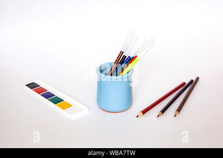 Blue vase for pencils on the white background with various pencils and paints Stock Photo