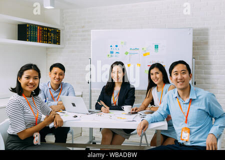 Group portrait of Asian business men and women smiling and looking at camera at company meeting room. Young business people at presentation together. Stock Photo