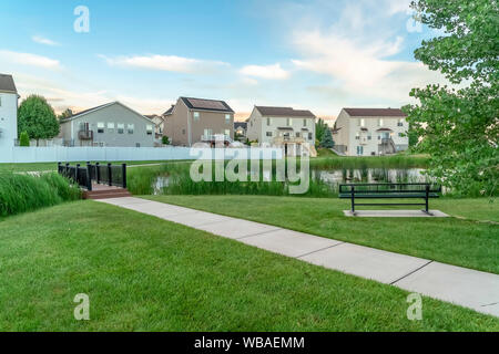 Neighborhood park with pond bridge pathway bench and trees in front of homes Stock Photo