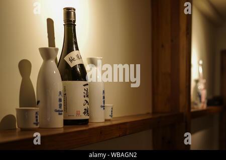 Shanghai, China - May 25, 2016: Kamotsuru Itteki Nyukon sake bottle with porcelain pots and cups set on wood shelf Stock Photo