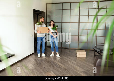 Positive young couple in casual outfit holding plants and box Stock Photo