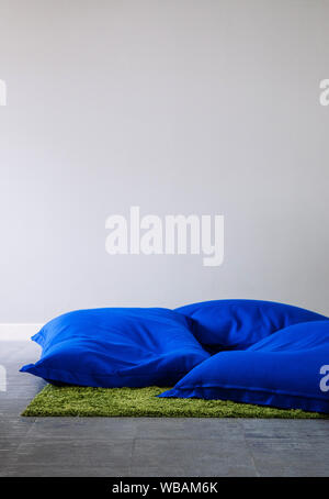 Blue bean bags on concrete floor with green carpet rug and white wall copy space background. Stock Photo