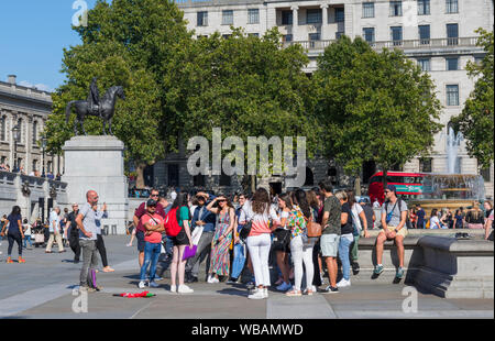 Group of tourists on a guided tour in Summer in Trafalgar Square, Charing Cross, Westminster, Central London, England, UK. Stock Photo