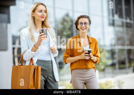 Portrait of a two young businesswomen walking with coffee near the office building outdoors Stock Photo