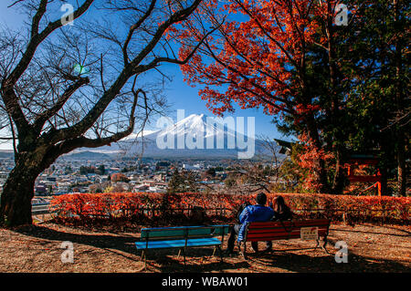 NOV 30, 2018 Fujiyoshida, Japan - Mount Fuji and red maple tree with sweet tourist couple sit on bench  at Chureito Pagoda Arakurayama Sengen Park Fuj Stock Photo