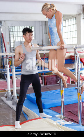 Man securing woman who doing exercises on  parallel bars in gym Stock Photo