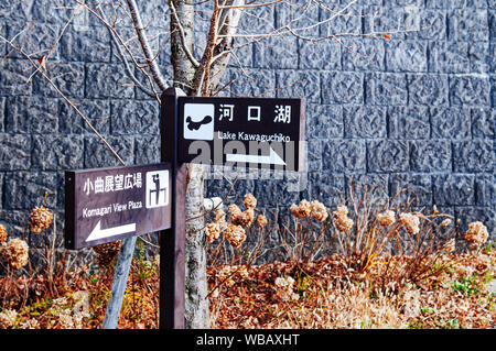 NOV 30, 2018 Kawaguchiko, Japan - Lake Kawaguchiko and Komagari View Plaza wooden sign direction information with garden and stone wall background Stock Photo