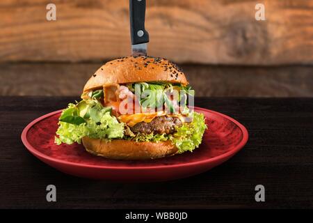 Original served beef burger on red plate with knife. Wooden table background. Fast food restaurant design concept.