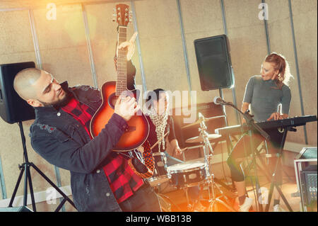 Bearded guy soloist playing the guitar and singing with two girls of his music band at studio Stock Photo