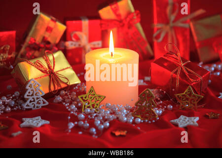 Burning candle in front of wrapped presents, decorated with pearls. Switzerland Stock Photo