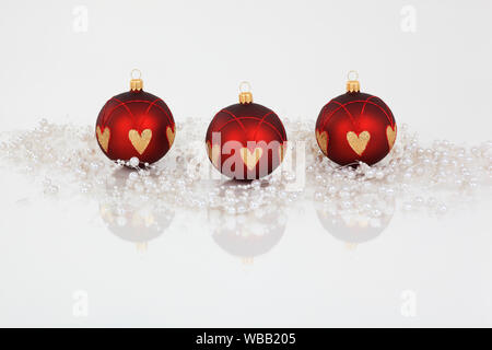 Three Christmas baubles in red and gold, surrounded by a string of pearls. Studio picture against a white background. Switzerland Stock Photo