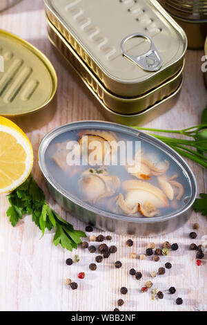 Canned seafood, whole shelled clams served on wooden table with parsley and pepper Stock Photo