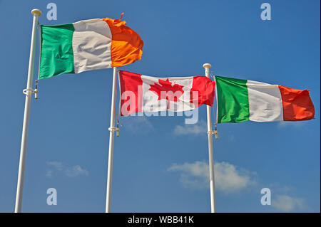 The flags of Italy, Canada and Republic of Ireland (Eire)flying on flagpoles against a blue sky. Stock Photo