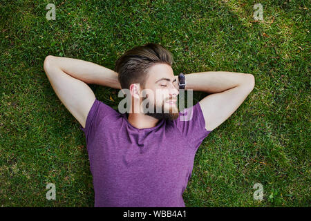 Young man lying on the grass in a park and relaxing with closed eyes Stock Photo