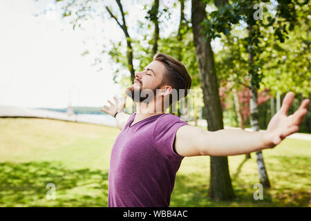 Young man extending arms and enjoying the sun outdoors in the park Stock Photo