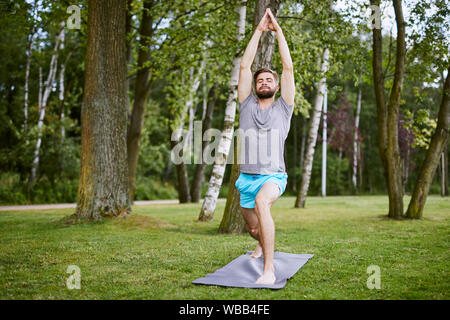 Focused young man doing yoga pose in the park in the morning Stock Photo