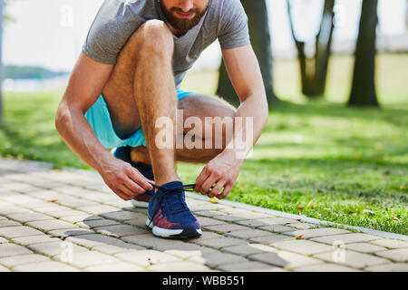 Close-up of man in sports clothing tying  shoelace outdoors Stock Photo