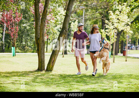 Young couple running and playing with their dog outdoors in the morning Stock Photo