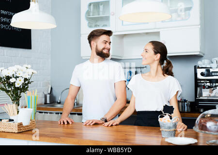 Couple of young small business owners looking at each other while standing behind counter in their cafe Stock Photo