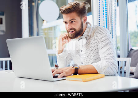 Handsome young man working on laptop while sitting in modern cafeteria Stock Photo
