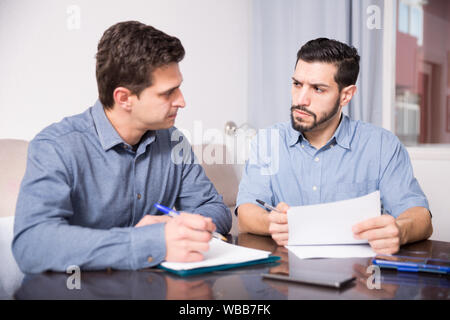 Two young men in serious discussion at home table while analysing documents together Stock Photo