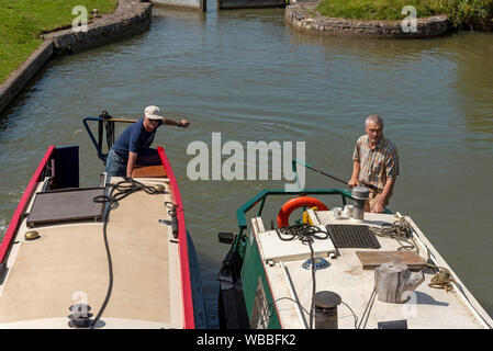 Devizes, Wiltshire, England, UK. August 2019.  Two narrowboat skippers holding the tillers of their boats as they enter a lock on the Kennet and Avon Stock Photo