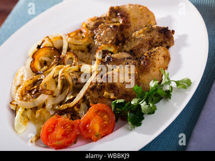 Rabbit liver roasted in breadcrumbs served with fried onion, tomatoes and parsley on white dish Stock Photo