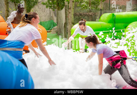 Friendly multiracial team having funny competition in collect of balls in inflatable foam pool on adults bouncy playground Stock Photo