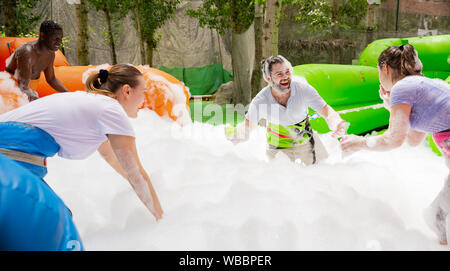 Friendly multiracial team having funny competition in collect of balls in inflatable foam pool on adults bouncy playground Stock Photo
