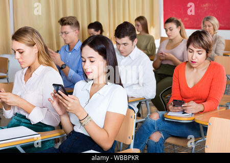 Serious students using smartphones to find necessary information on lecture in university class Stock Photo