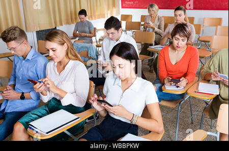 Diligent serious students using smartphones to find necessary information on lecture in university class Stock Photo